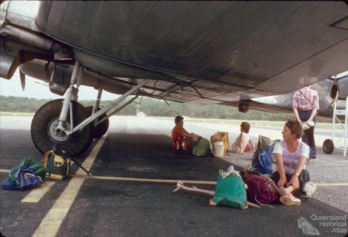 Passengers sitting in the shade of an Air Queensland DC3, Lockhart Airport, 1982